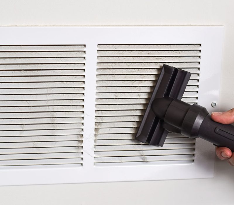 Person's hand vacuuming dirty return air vents